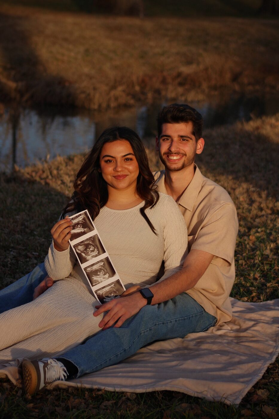 Couple sitting in a field holding ultrasound photo